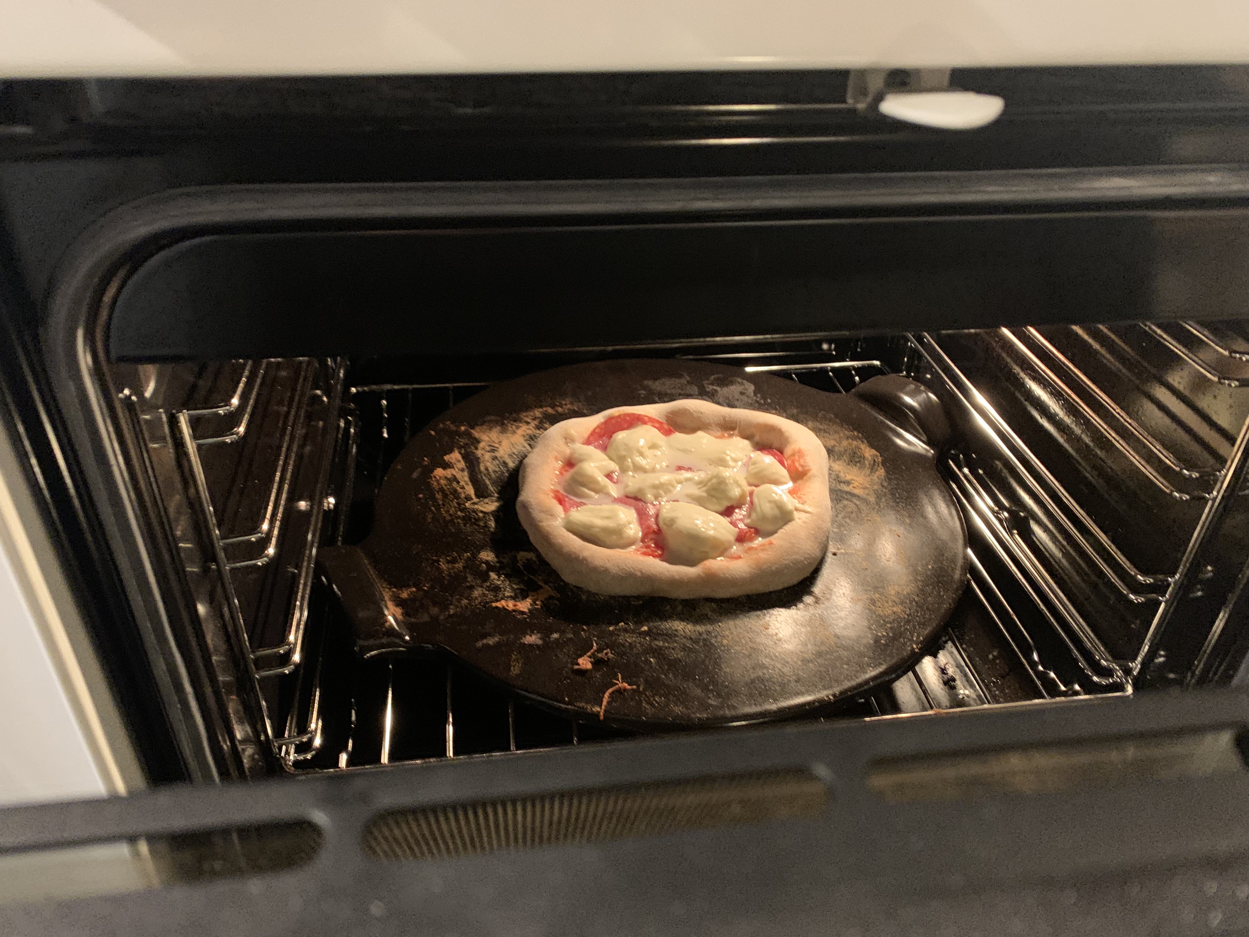 Self-made pizza warming in the oven using a pizza stone